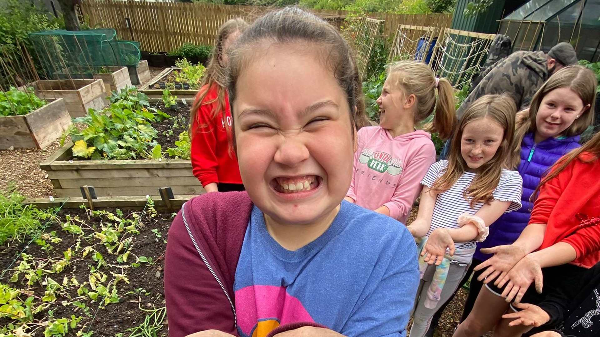 A child smiling and showing her muddy hands to the camera in a community garden